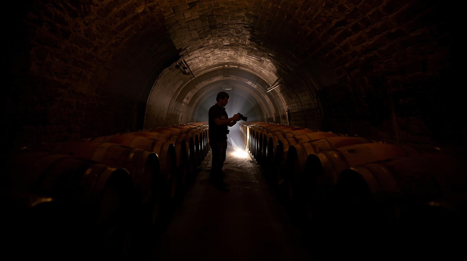Photographer capturing images inside a wine cave on Spring Mountain in Napa Valley, with rows of oak barrels aging Cabernet Sauvignon.