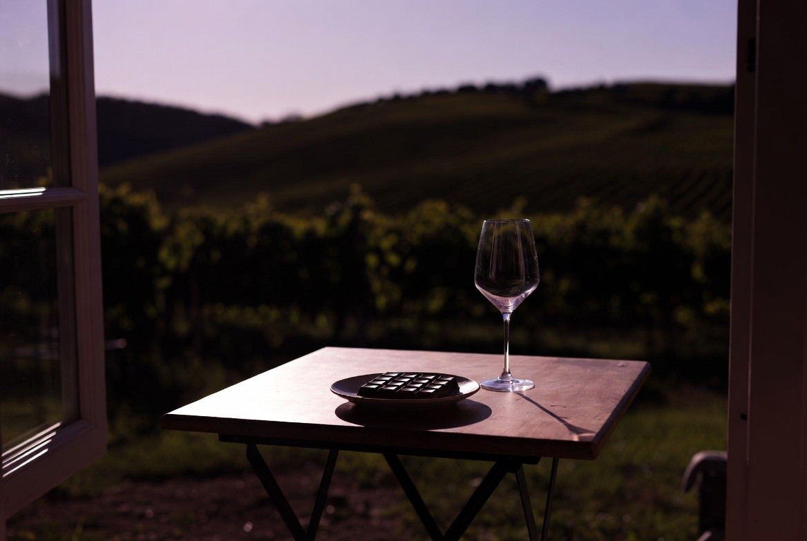 Dark chocolate square paired with a glass of Napa Valley red wine on a table at dusk, showing a calm evening dessert moment in the vineyard.