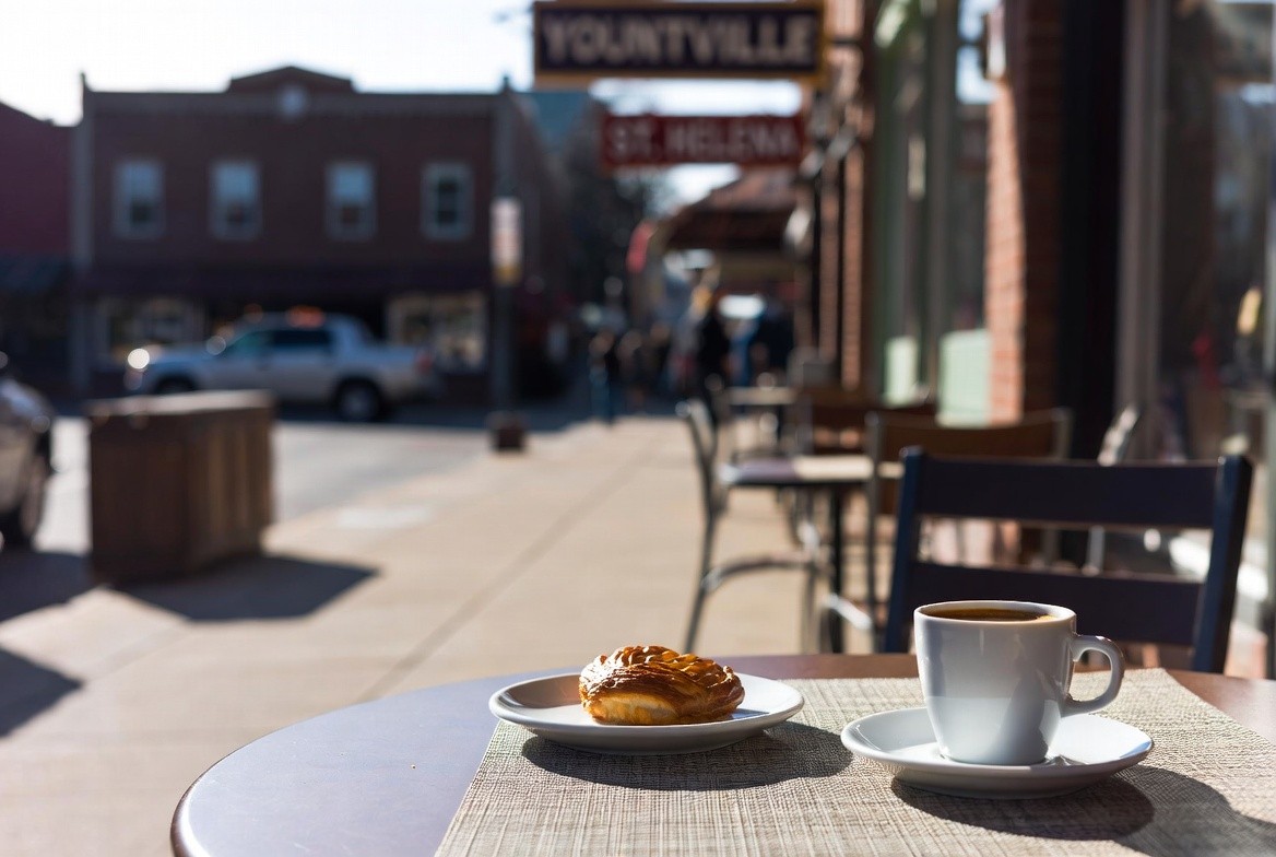 Pastry and coffee on a sidewalk table in a Napa Valley town during a quiet early morning before shops and wineries open.
