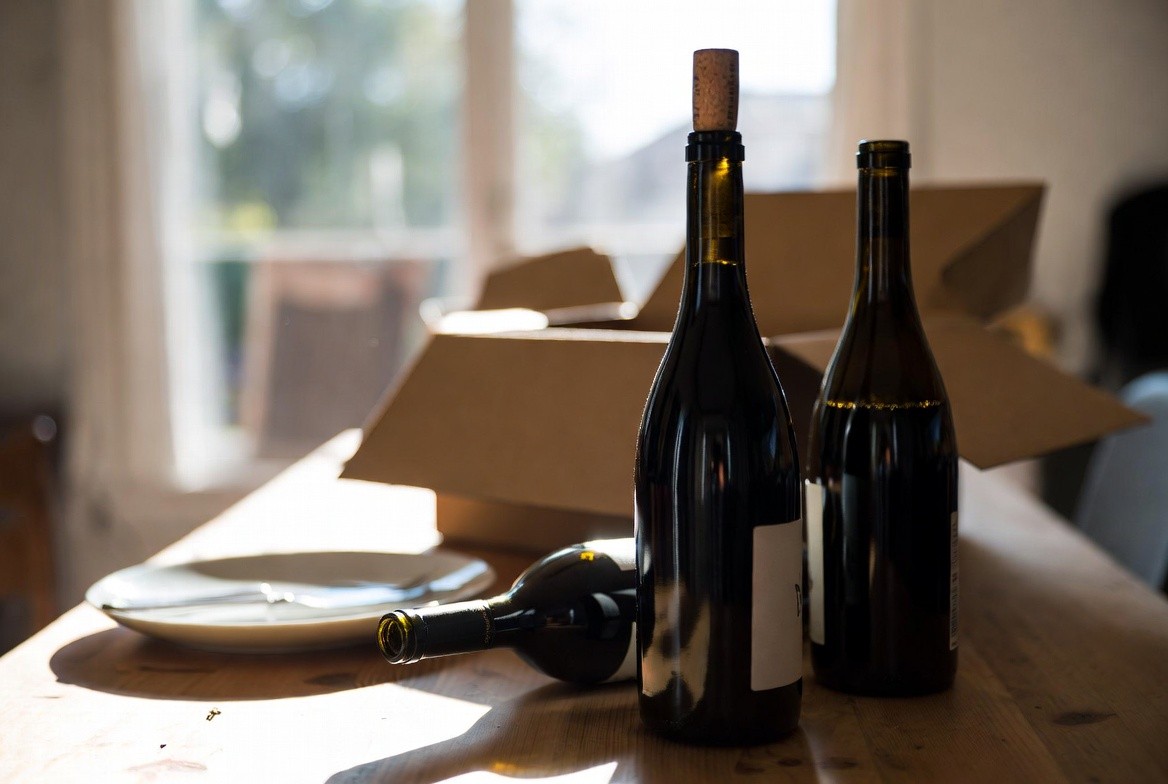 Napa Valley wine club shipment opened at home with three bottles on a wooden table in natural light, suggesting connection to the winery beyond the visit.